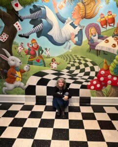 Artist Kathi Ember sits with her "Alice in Wonderland" mural
